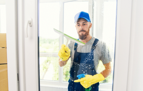 c08db694 male janitor using squeegee clean window office wearing apron gloves as he works 1